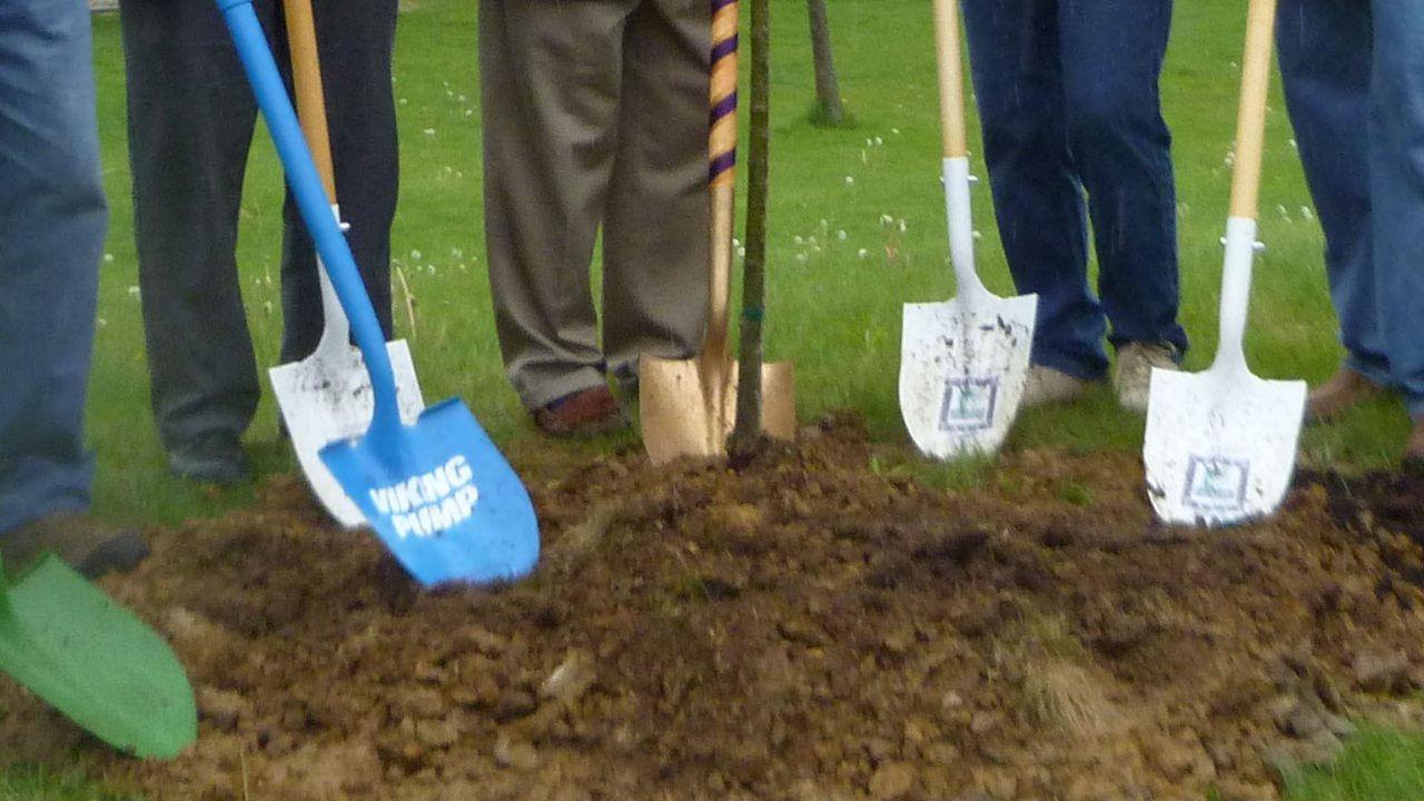 People holding shovels after planting a young sapling.
