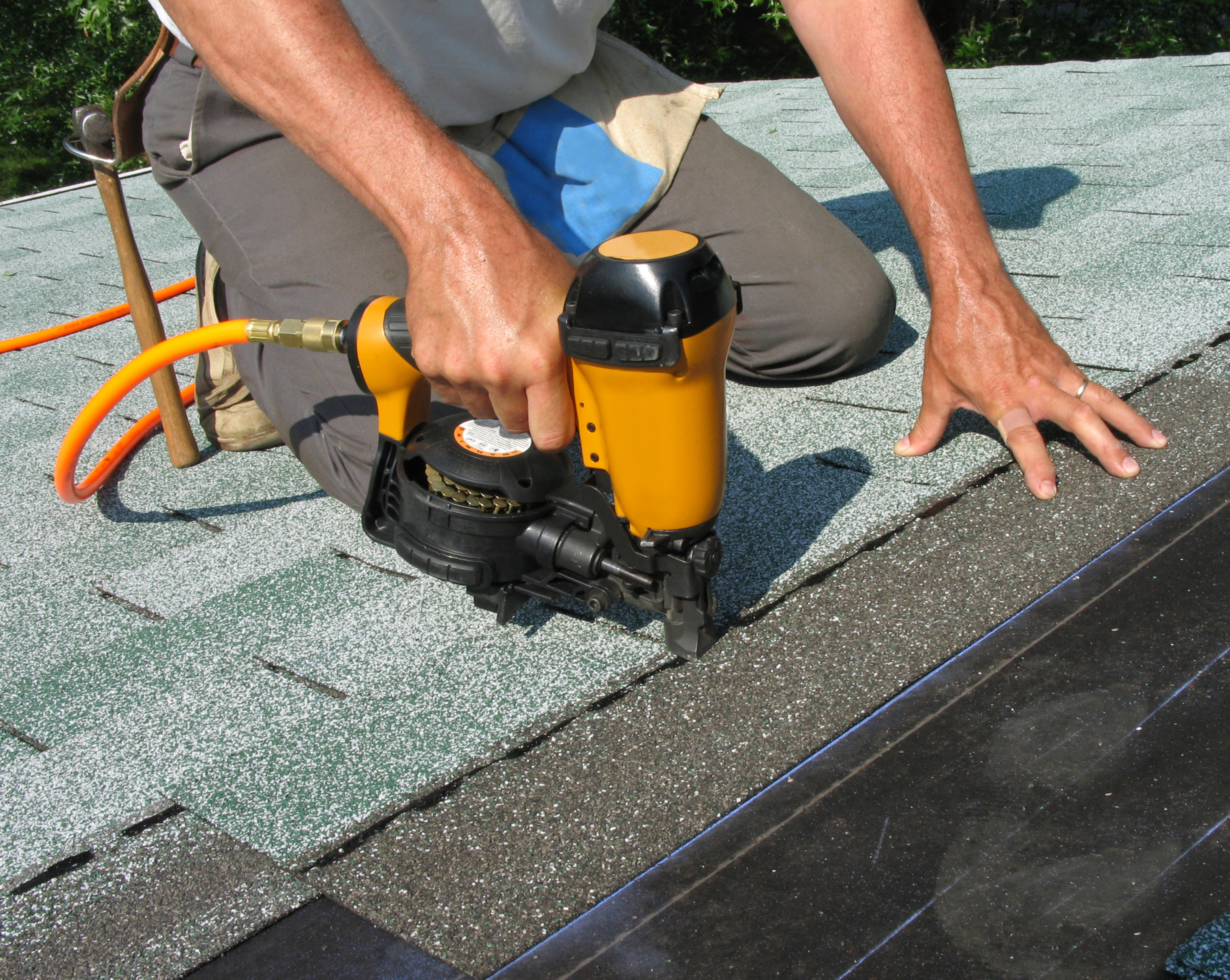 Worker on a roof installing asphalt shingles with a nail gun