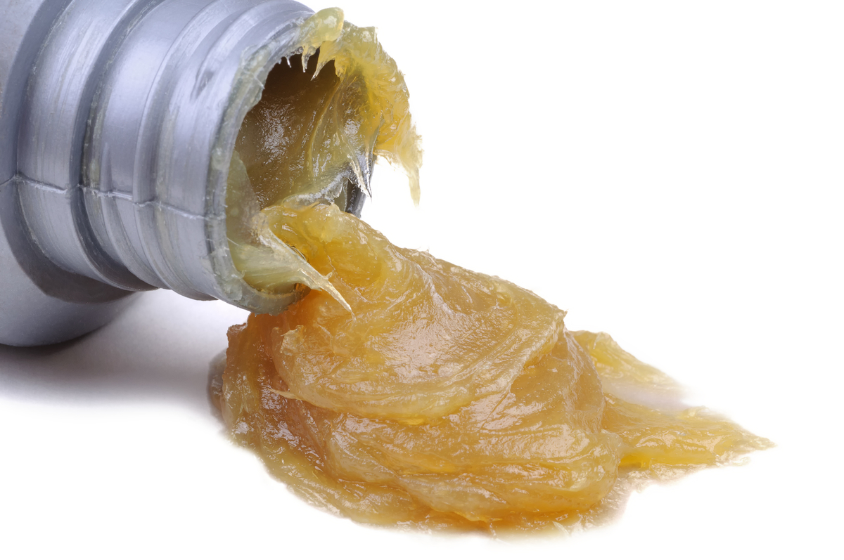 bottle of thick grease tipped over with grease pooling out of it