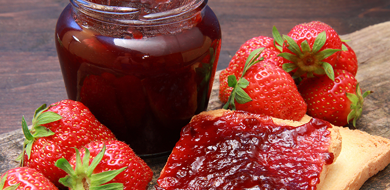 Jam in a jar and strawberries surrounding it