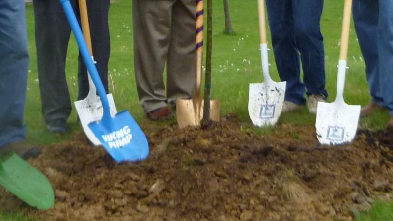 People holding shovels after planting a young sapling. 