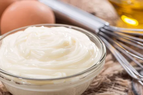Mayonnaise in a small glass bowl next to a whisk and eggs
